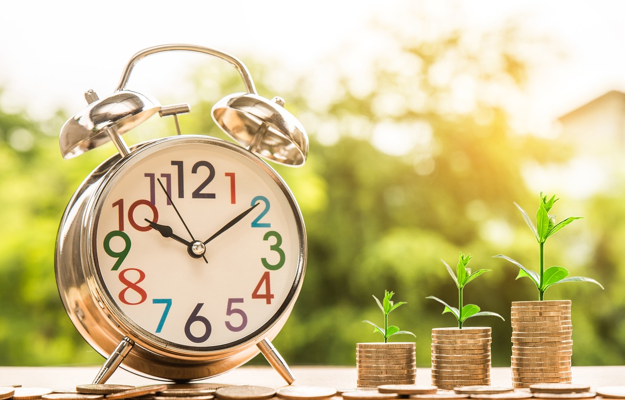 Monedas apiladas con un reloj despertador a lado